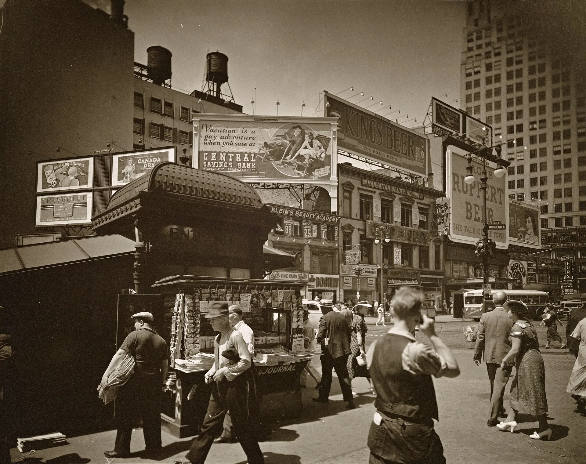 * Code: I.B.; III.B.1. Men and women hurry past newstand outside uptown subway entrance, street beyond is lined with businesses topped with large billboards. Citation/Reference: CNY# 151